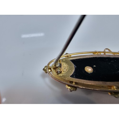411 - A vintage 9ct yellow gold brooch inset with a large oval black onyx stone with a floral and split se... 