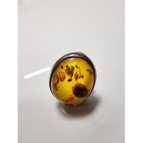 389 - A large ornate sterling silver dress ring inset with a large natural Baltic amber cabochon with incl... 