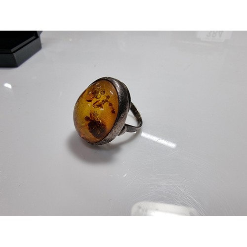 389 - A large ornate sterling silver dress ring inset with a large natural Baltic amber cabochon with incl... 