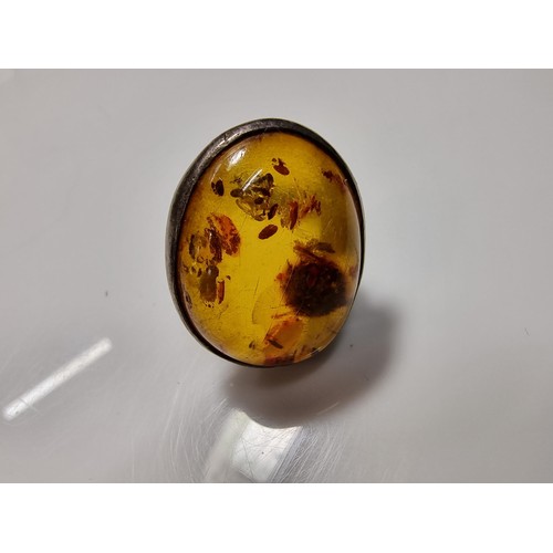 389 - A large ornate sterling silver dress ring inset with a large natural Baltic amber cabochon with incl... 