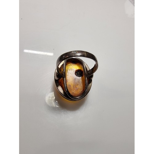 389 - A large ornate sterling silver dress ring inset with a large natural Baltic amber cabochon with incl... 
