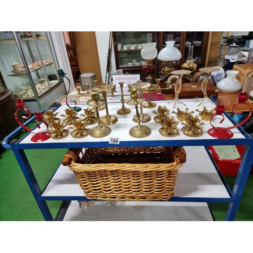 194 - A large quantity of various brass candlesticks all in a wicker basket with wooden handles.