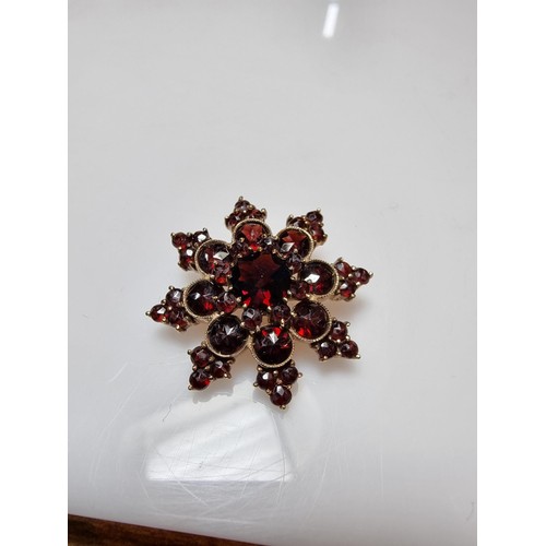 389 - A pretty hallmarked 9ct yellow gold brooch in the form of a star, inset with many garnet stones pres... 