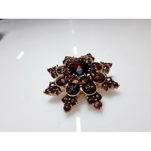 389 - A pretty hallmarked 9ct yellow gold brooch in the form of a star, inset with many garnet stones pres... 