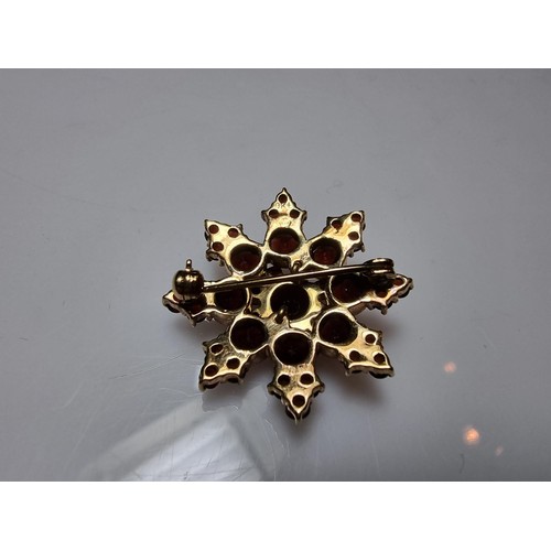 389 - A pretty hallmarked 9ct yellow gold brooch in the form of a star, inset with many garnet stones pres... 