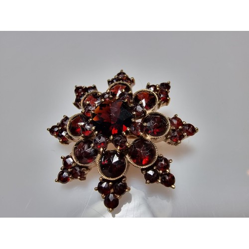 389 - A pretty hallmarked 9ct yellow gold brooch in the form of a star, inset with many garnet stones pres... 