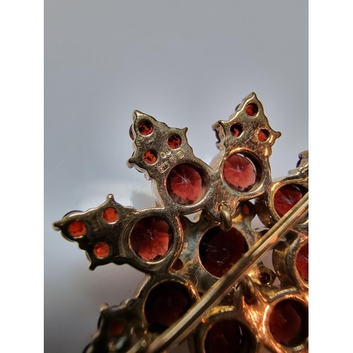 389 - A pretty hallmarked 9ct yellow gold brooch in the form of a star, inset with many garnet stones pres... 