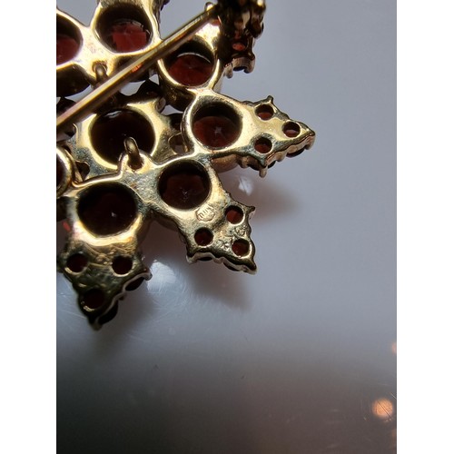 389 - A pretty hallmarked 9ct yellow gold brooch in the form of a star, inset with many garnet stones pres... 