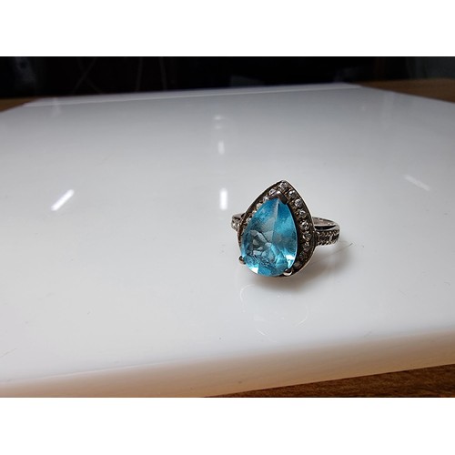 359 - An ornate 925 silver dress ring inset with a large blue glass stone surrounded by smaller CZ crystal... 