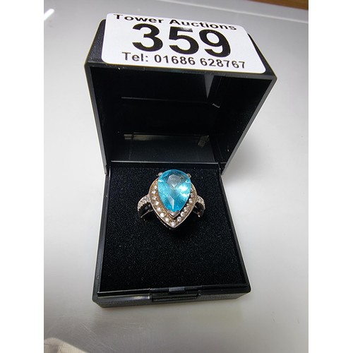 359 - An ornate 925 silver dress ring inset with a large blue glass stone surrounded by smaller CZ crystal... 