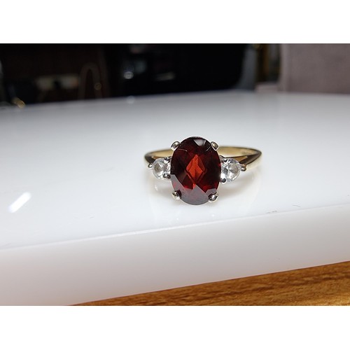 394 - An as new hallmarked yellow gold dress ring inset with a oval faceted garnet gemstone with 2 CZ crys... 