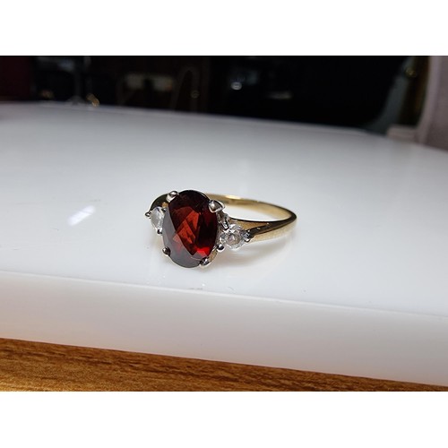 394 - An as new hallmarked yellow gold dress ring inset with a oval faceted garnet gemstone with 2 CZ crys... 