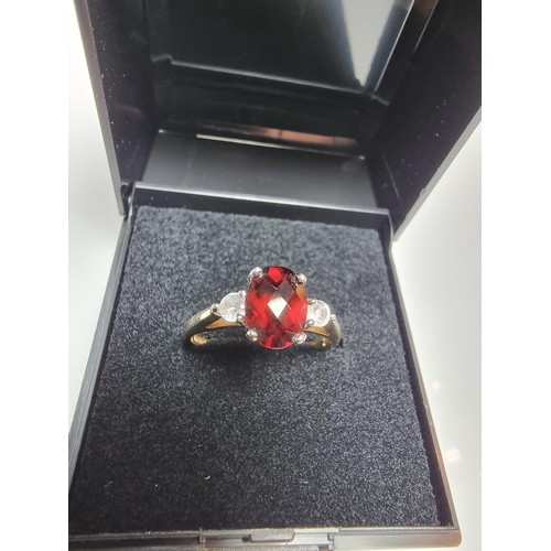 394 - An as new hallmarked yellow gold dress ring inset with a oval faceted garnet gemstone with 2 CZ crys... 