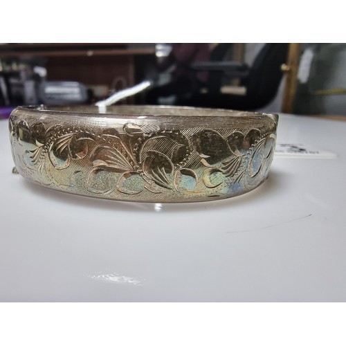 373 - A vintage hallmarked silver hinged bangle with an ornate engraved floral design to one side, complet... 