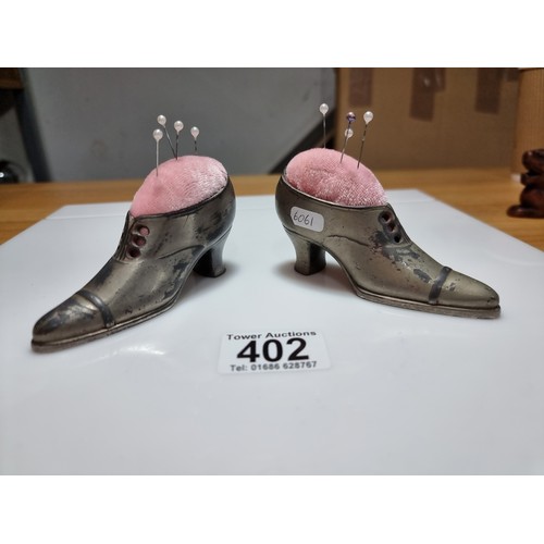 402 - A pair of metal shoe formed pin cushions with a quantity of pins in good clean condition. Height of ... 