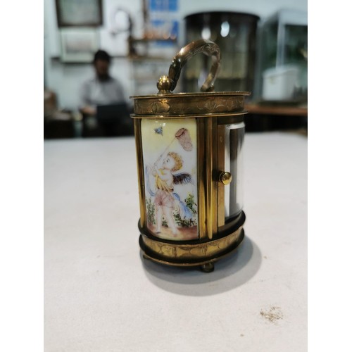 245 - Vinatge brass mini oval shaped carriage clock with porcelain sides depicting cherubs one panel to th... 