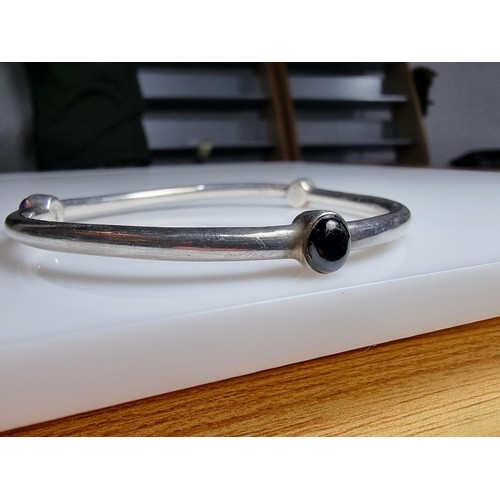 272 - A solid 925 silver bangle inset with 3 different coloured stones, red, purple and black. In excellen... 