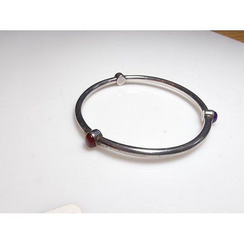 272 - A solid 925 silver bangle inset with 3 different coloured stones, red, purple and black. In excellen... 