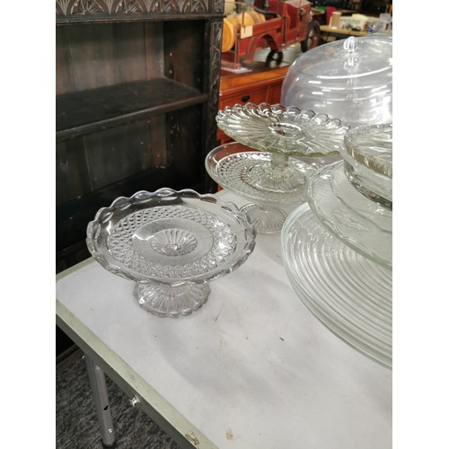 22 - A large quantity of catering glass cake stands of various sizes along with a quantity of cake domes,... 