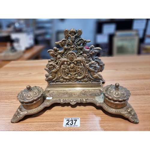 237 - A Victorian ornate brass desk stand and double inkwells featuring an ornate cherub design in good cl... 