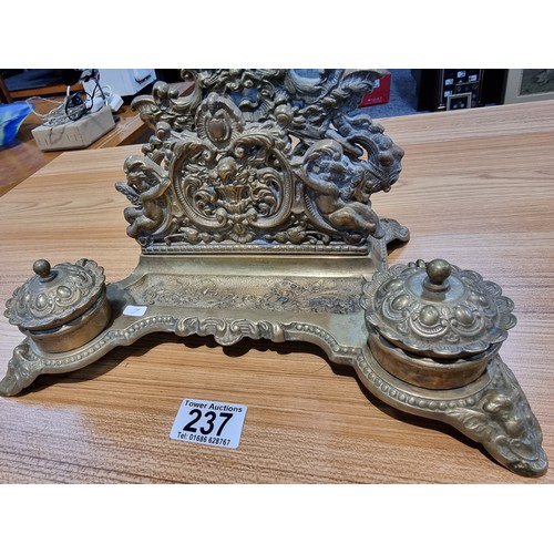 237 - A Victorian ornate brass desk stand and double inkwells featuring an ornate cherub design in good cl... 