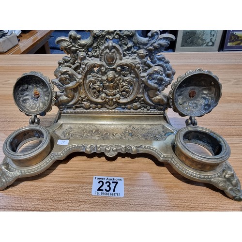 237 - A Victorian ornate brass desk stand and double inkwells featuring an ornate cherub design in good cl... 