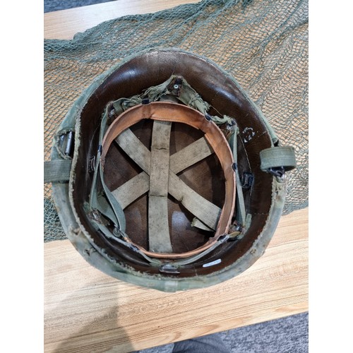 238 - A vintage military helmet with a green mesh netting, has marking to the inside of the helmet. Please... 