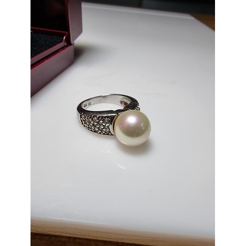 323 - A 925 silver dress ring inset with a large faux pearl and a quantity of CZ crystal stones, in good c... 
