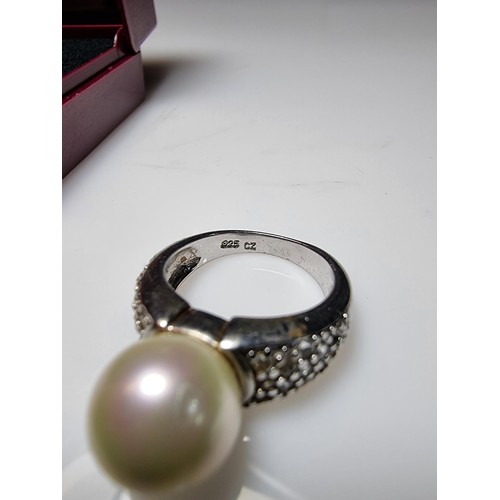 323 - A 925 silver dress ring inset with a large faux pearl and a quantity of CZ crystal stones, in good c... 