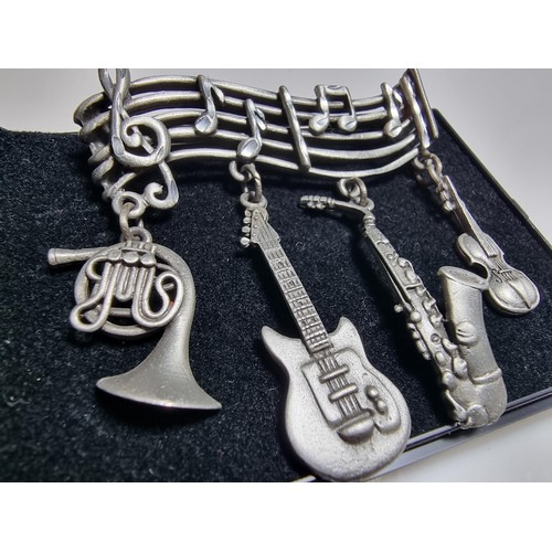 229 - An unusual music related pewter brooch featuring 4 drops which are different instruments presented o... 