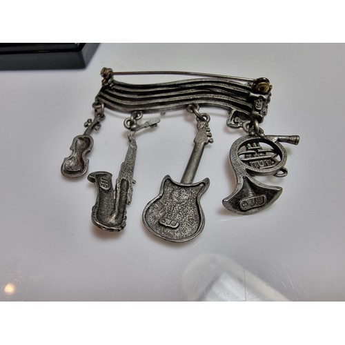 229 - An unusual music related pewter brooch featuring 4 drops which are different instruments presented o... 