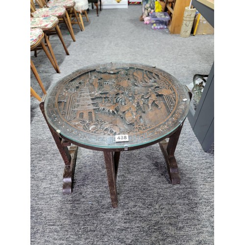 488 - Hand carved camphor wood round table with glass top and of a gate leg variety. Having detailed carvi... 