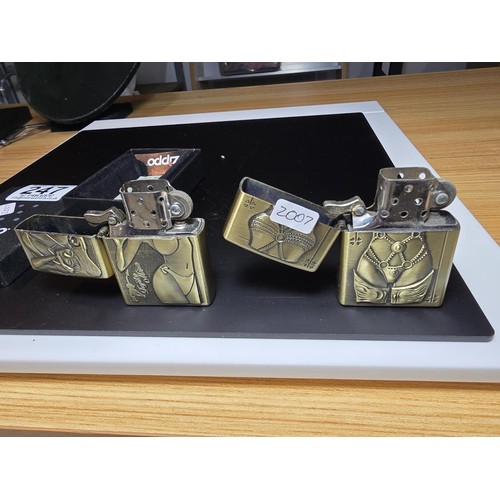 247 - A pair of Kantai brushed brass petrol lighters with bikini dressed women as the design. 1 lighter is... 