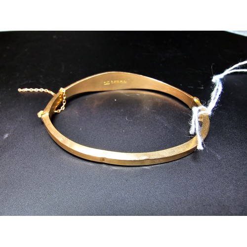 294 - A hallmarked 9ct yellow gold hinged bangle with safety chain, the bangle is missing a stone from the... 