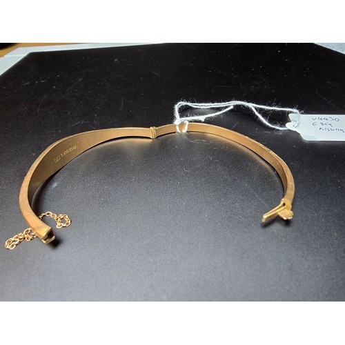 294 - A hallmarked 9ct yellow gold hinged bangle with safety chain, the bangle is missing a stone from the... 