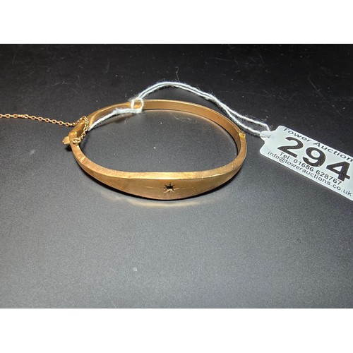 294 - A hallmarked 9ct yellow gold hinged bangle with safety chain, the bangle is missing a stone from the... 