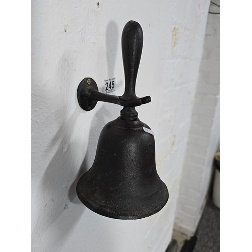 245 - An antique cast iron hand bell with a cast iron handle and a cast iron wall bracket marked Captain. ... 