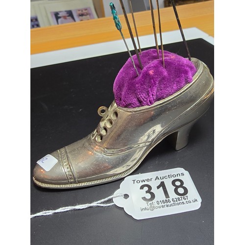 318 - A large metal shoe formed pin cushion containing a quantity of pins and hat pins which includes 2 go... 