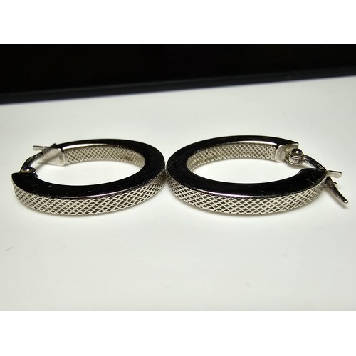 211 - Pair of hallmarked 9ct. white gold hoop earrings with a machine engraved design to the inside and ou... 