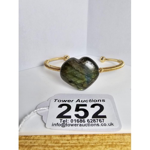 252 - A new and unused gold plated bangle inset with a heart shaped labradorite stone having excellent fla... 