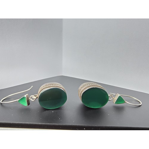 207 - A pair of large ornate and unusual sterling silver drop earrings featuring a polished green glass in... 