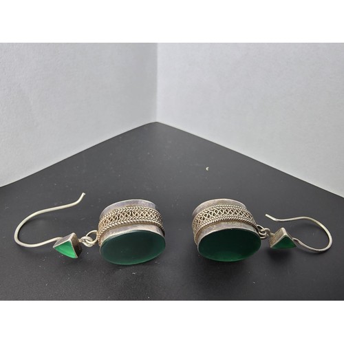 207 - A pair of large ornate and unusual sterling silver drop earrings featuring a polished green glass in... 