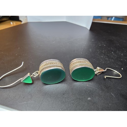 207 - A pair of large ornate and unusual sterling silver drop earrings featuring a polished green glass in... 