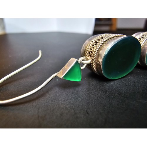 207 - A pair of large ornate and unusual sterling silver drop earrings featuring a polished green glass in... 