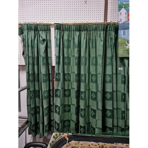 33 - A pair of green check curtains with a crest style  design on a brass curtain rail complete with hook... 