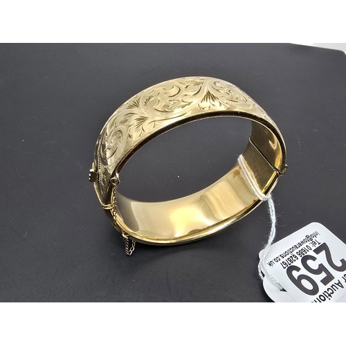 259 - A good quality ornate chunky rolled gold hinged bangle featuring an ornate engraved design on one si... 