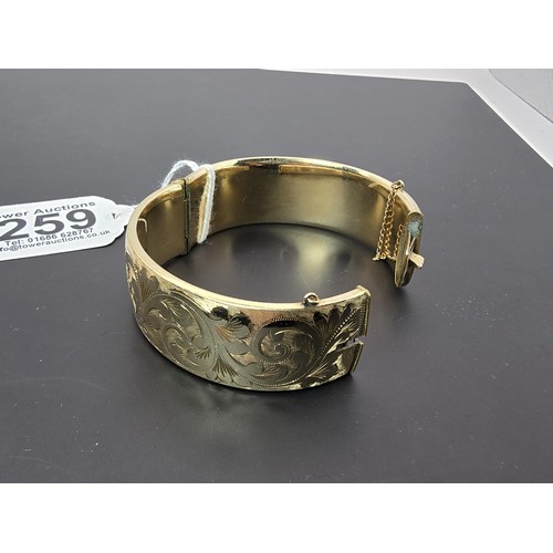 259 - A good quality ornate chunky rolled gold hinged bangle featuring an ornate engraved design on one si... 