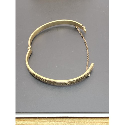 247 - A vintage 9ct yellow gold with metal core hinged bangle having an engraved design to one side, clasp... 