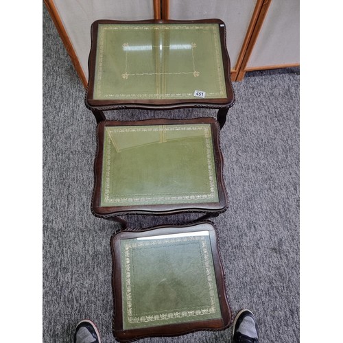 451 - A nest of 3 side tables, In mahogany with a green leather inlay and glass cover. One leg loose needs... 