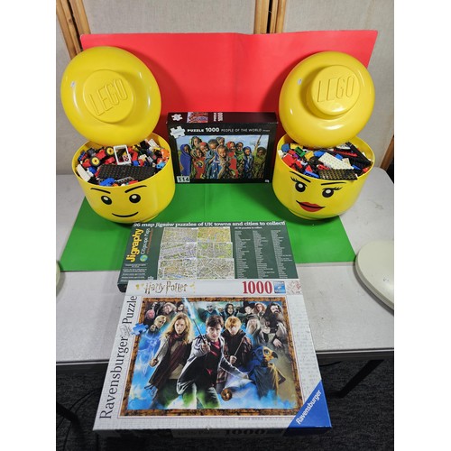 114 - 2x original Lego containers in the form of Lego heads both full of Lego pieces along with 3x jigsaws... 